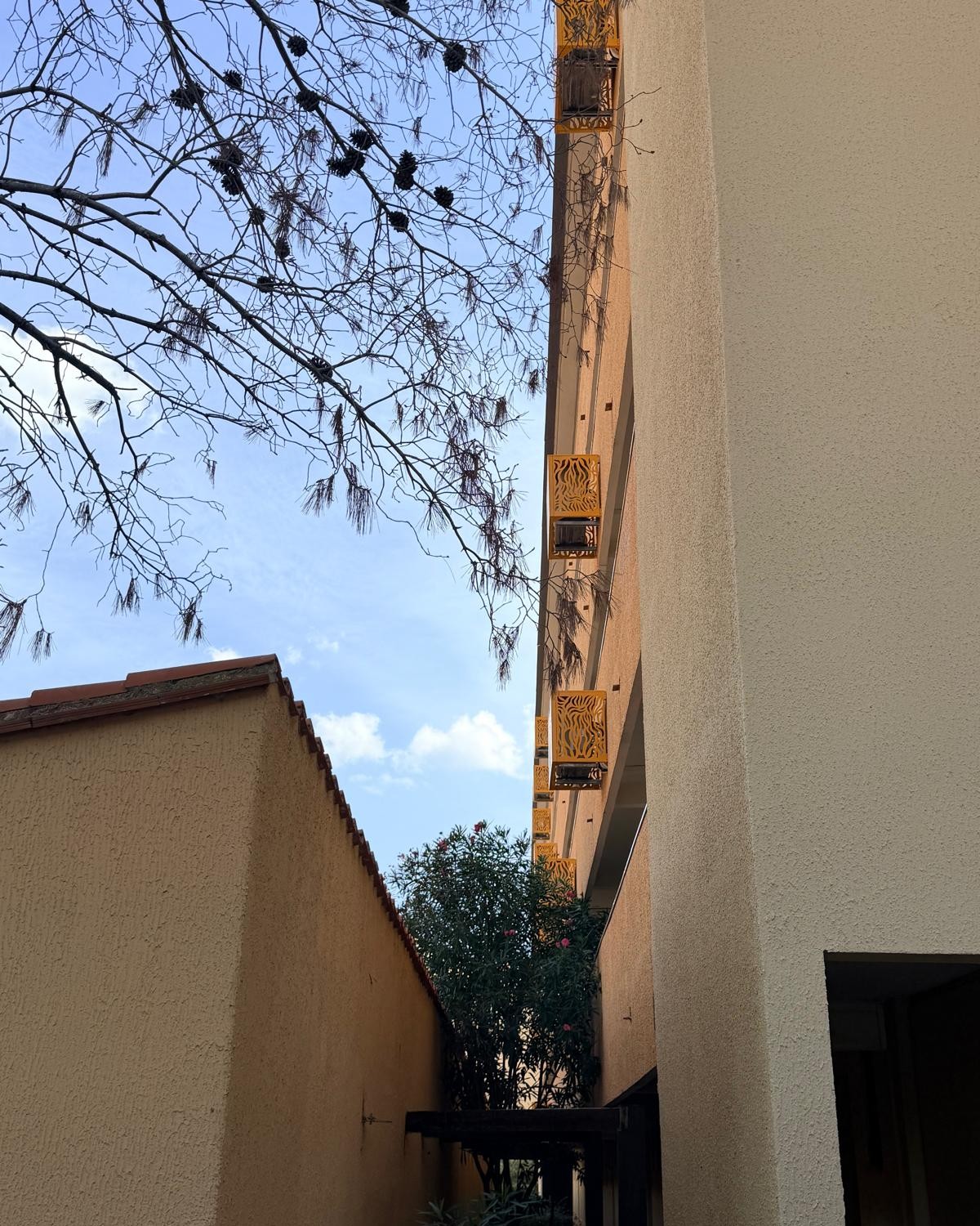 Vue en contre-plongée d'une ruelle montrant l'alignement des cache-clim sous les balcons