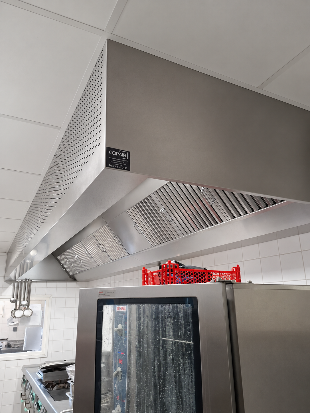 Hotte d'extraction professionnelle Copair en inox avec filtres à chicane, installée au-dessus d'un équipement de cuisine dans un restaurant