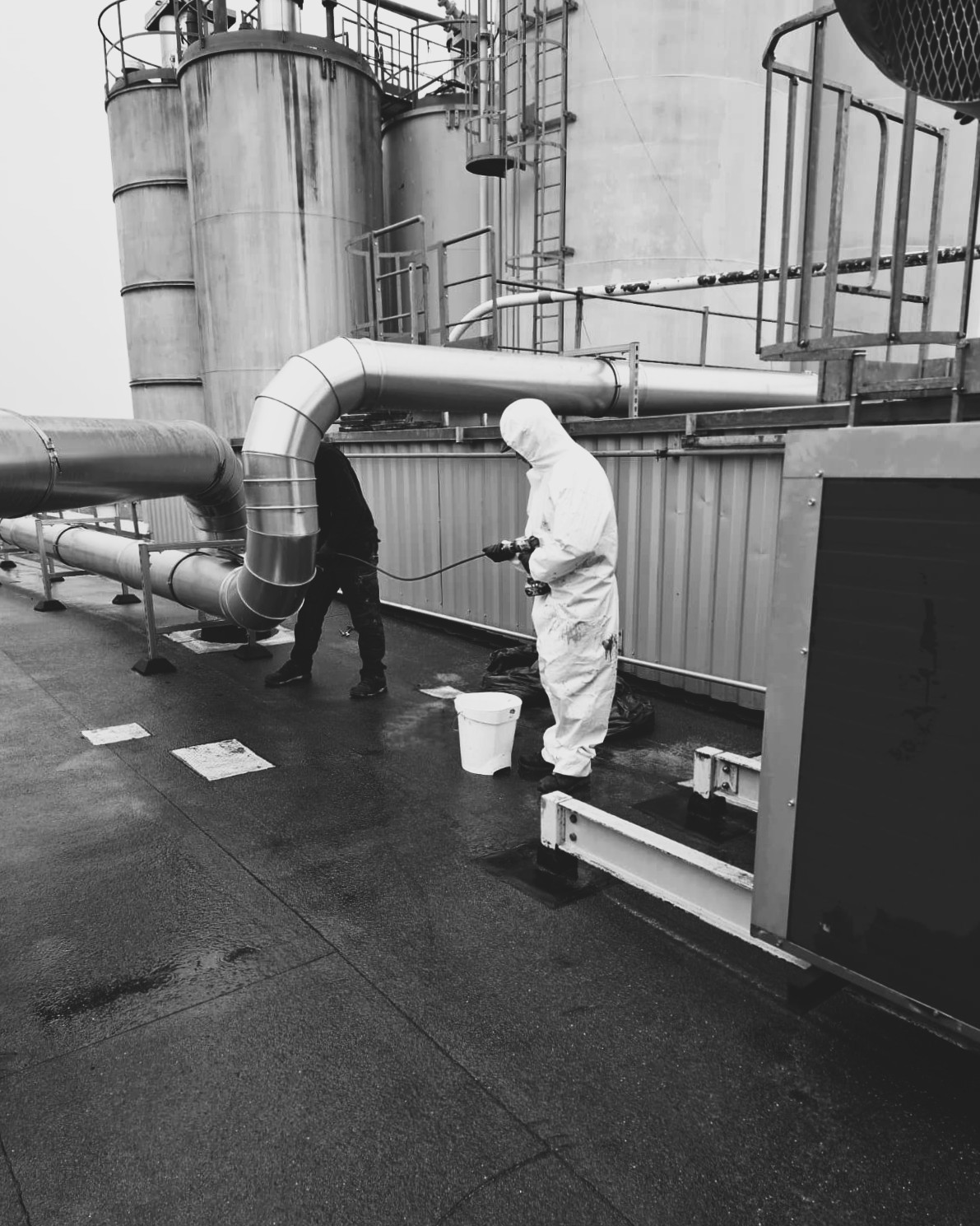 Techniciens réalisant le nettoyage de surfaces d'une cabine sur toiture près de cuves industrielles
