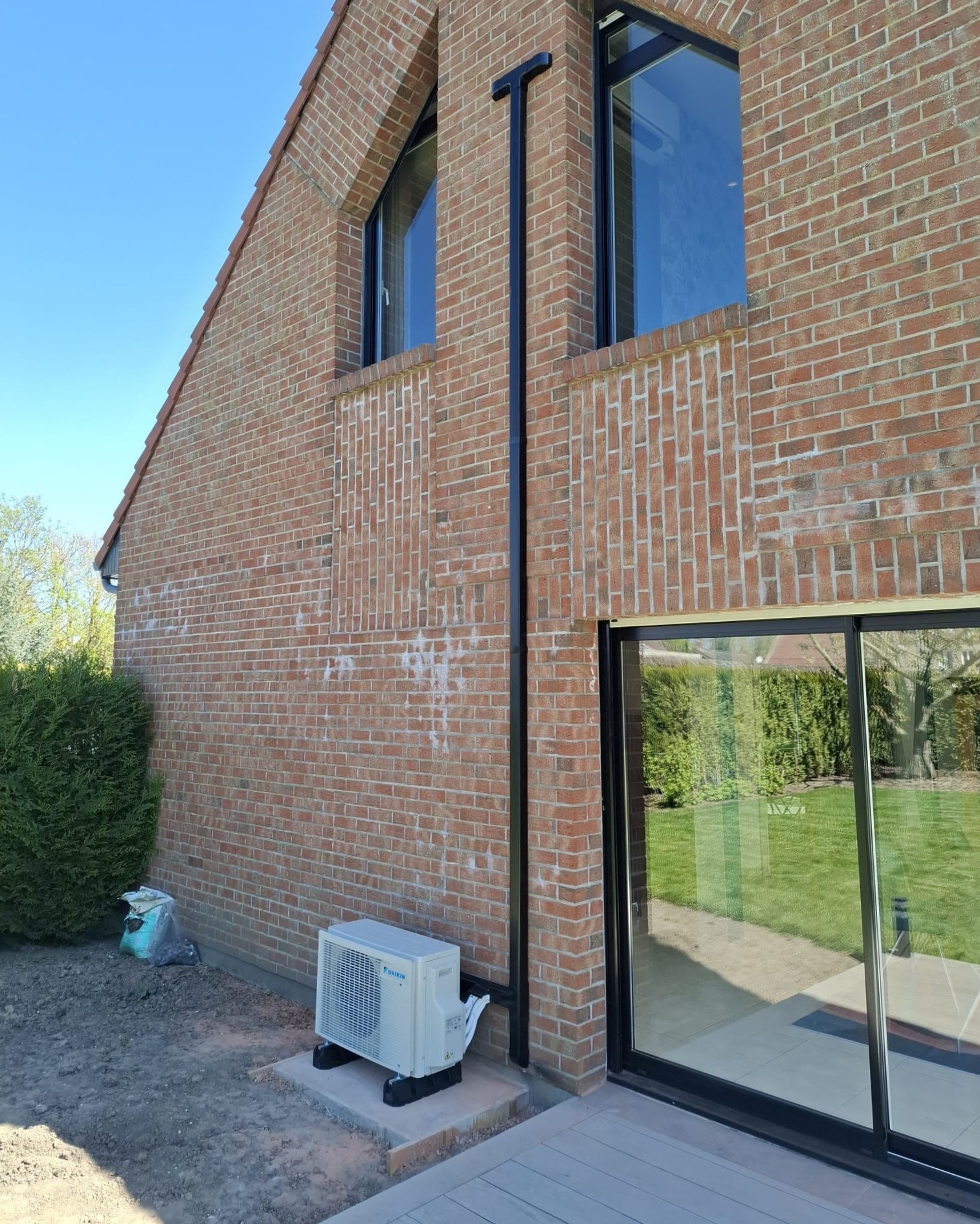 Groupe extérieur du bisplit Daikin Stylish au pied d’une façade en brique, avec liaisons en goulotte noire