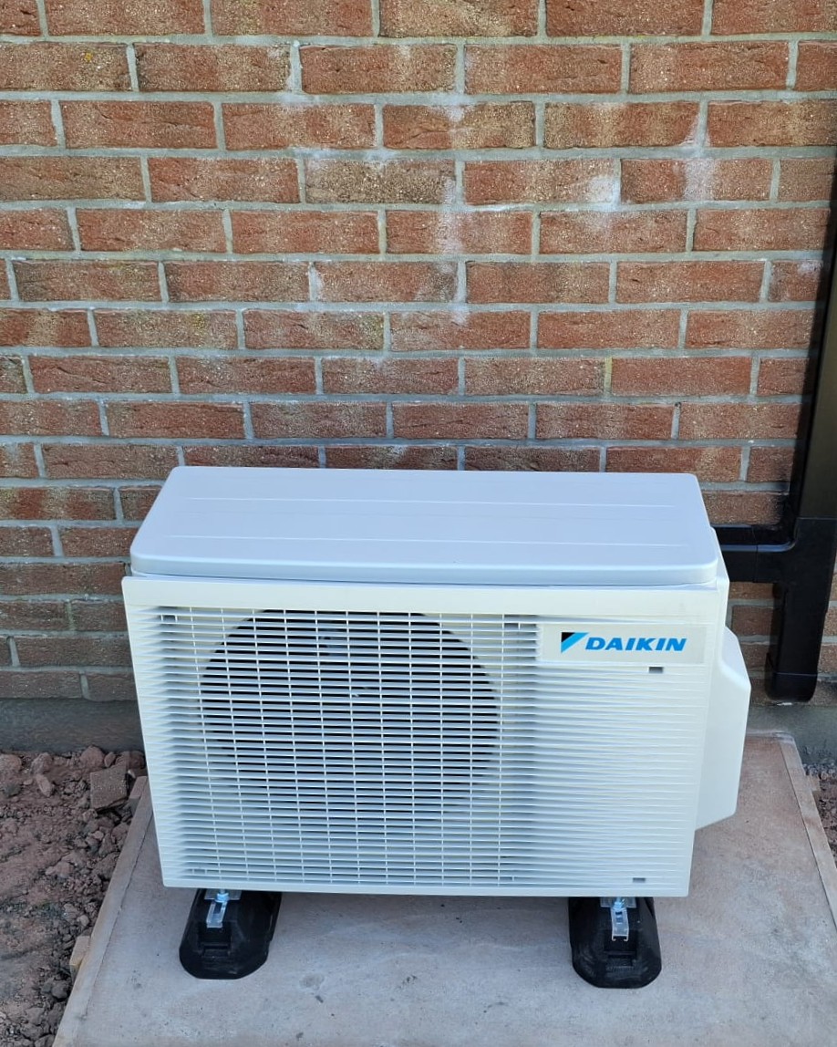 Groupe extérieur Daikin posé sur dalle et supports anti-vibratiles contre un mur en brique