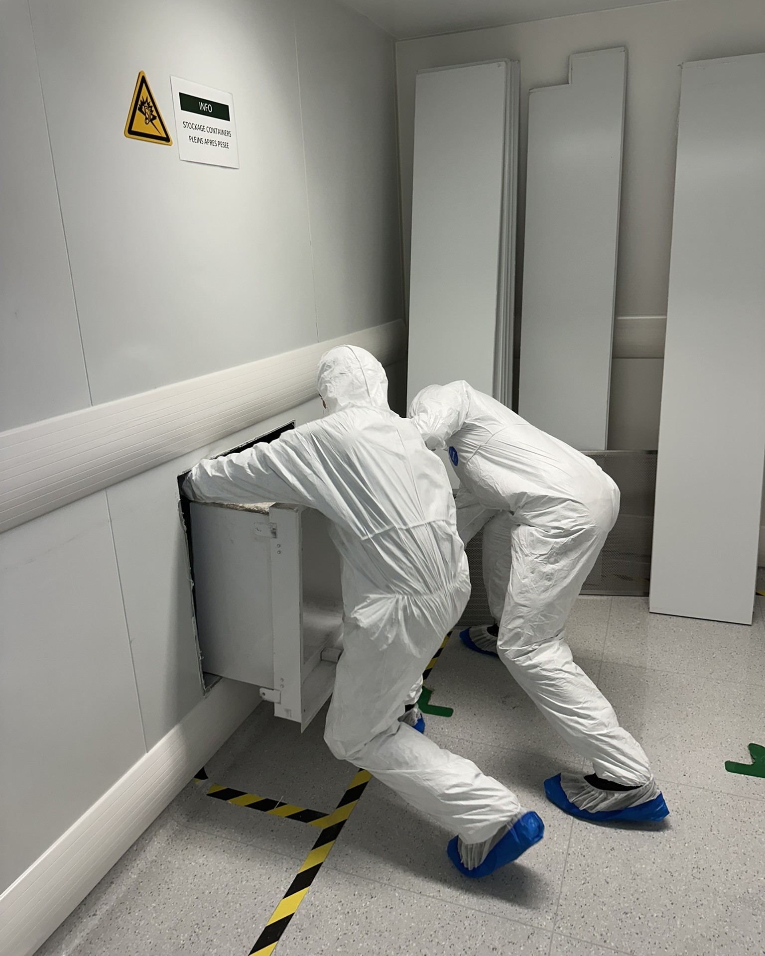 Deux techniciens en combinaison de protection intervenant sur un caisson technique en salle propre pharmaceutique